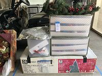 Box and stacked storage totes with tags on them showing the contents and brand of the Christmas tree and storage totes.