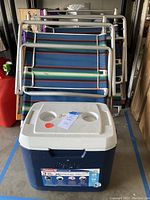Photo of two folded striped metal frame beach chairs and one blue and white Coleman cooler with lid and cup holders