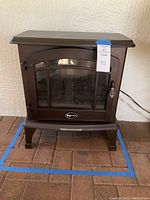 Full view of the brown Comfort Glow electric fireplace stove on a brick floor, showing front glass door and body shape.
