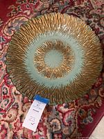 Top view photo of round decorative plate showing textured gold pattern and blue-green glaze.