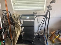 Photo of metal golf caddy storage, golf clubs, bag, and golfer figurine placed in a garage against a white wall under a window.