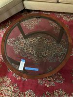 Top view showing round coffee table with wood rim and clear glass top placed on patterned carpet.