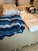 Two king size blankets, one packaged beige color and one crocheted blue and white on a bed
