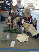 Wide view of seven Santa figures, PEACE sign, wreath light, ceramic plate, and small bag with decoration