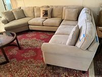 Full view of L-shaped beige sectional sofa with wedge on left, center section, straight sofa on right, on red patterned rug