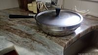 Photo of the deep stainless steel braiser with lid and black knob on counter