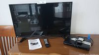 Photo showing 32-inch Sylvania flat screen TV, TV remote, instruction manual, and Sony CD/DVD player with remote on wooden surface.