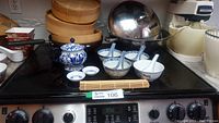 Full view of all items set on stove showing stacked bamboo steamers, wok pan with lid, bowls with spoons, teapot, saucers and bamboo mat.