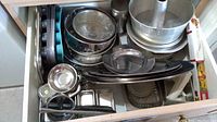 Drawer with stacked metal bakeware including pie plates, round pans, loaf tins and graters