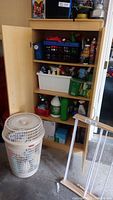 Wooden cabinet with two plastic bins filled with assorted cleaning supplies and liquids, white laundry hamper in front
