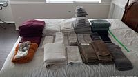 Photo of bathroom towels of different colors and sizes arranged on a bed in stacks