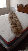 Full length view of long mink stole laid flat on mattress showing fur texture and color.