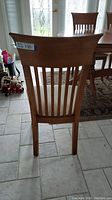 Rear view of one hardwood dining chair showing high curved back with vertical slats on tiled floor.
