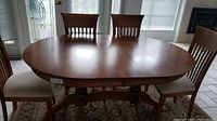Front view of the extended hardwood dining table with three removed leaves attached, showing the wood grain and oval shape.