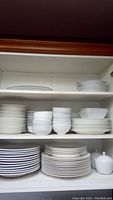Shelves containing multiple stacks of white porcelain and fine bone china plates and bowls in various sizes.