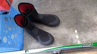 Close-up of black neoprene water boots with red interior and sole details alongside parts of the Ashlan brand fly fishing rod.