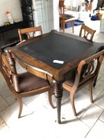 Square mahogany games table with black playing surface and four chairs around it on tile floor.