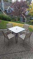 Outdoor square table with clear glass top and metal frame, four matching chairs with mesh seating.