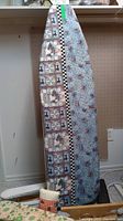 Photo showing upright ironing board with two distinct fabric covers in cat patchwork and blue sewing themed prints.