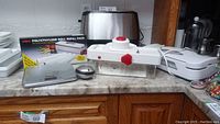 Photo showing Polysave polyethylene roll refill pack box, manual slicer, metallic digital kitchen scale, and mechanical timer on countertop.
