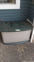 Closed Rubbermaid outdoor storage bin in green/tan against house exterior.
