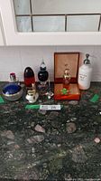 Multiple perfume bottles, small jeweler bowl, floral brooch, mouse metal ring holder, and a ceramic dispenser on a kitchen counter.