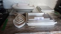 White ceramic or porcelain rectangular, oval and square serving plates and platters stacked and nested on a countertop.