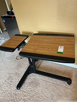 Front view of adjustable mobile laptop desk with two wood finish platforms and black metal frame on caster wheels.
