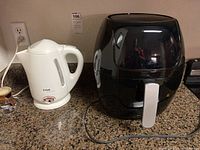 Power XL black air fryer and white T-Fal electric tea pot both plugged in on countertop.