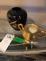 Two Asian vases on a glass table, one black with gold floral design and one gold with two handles