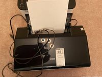 Top view of black Epson printer with paper loaded and power cable attached.