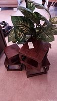 Full view of four wooden plant stands stacked together, showing medium brown stain and open shelf design, one stand with damage.