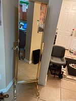 Front view of the full-length brass-colored standing floor mirror reflecting part of the room.
