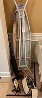 Ironing board folded against the wall with three appliances on the floor beside it