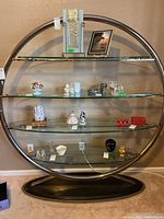 Full view of the round chrome and glass etagere wall unit showing all 4 glass shelves and wooden base with some displayed small items (not included)