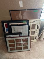 Photo showing assortment of frames leaning against a wall including large black frame, white multi-section frame, and detailed cream-colored frame