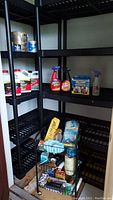 Two black plastic shelving units with various household items and a metal wire cart on wheels filled with cleaning and storage products.