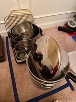 Stacked metal pots with black handles and lids, a cooling rack and a white microwave plate behind