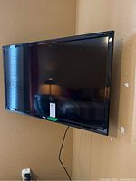 Black RCA flat screen television mounted on beige wall showing front screen and surrounding area.