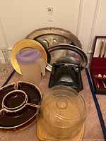Photo of all items together showing metal platters, gold chargers, ceramic divided appetizer dish, plastic pitcher, and wood plate with glass dome lid.