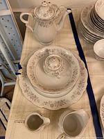 Full view of tea pot, serving plate, smaller dishes, and creamer showing floral silver design and white china