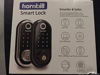Photo of the front packaging showing the Hornbill smart lock in black and silver, highlighting features like key free, app control, anti-theft alert, auto-lock, micro USB backup, IC card, and fingerprint.
