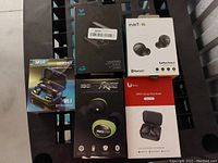 Top view of five different wireless earbud boxes on a bench showing brand names and packaging details.