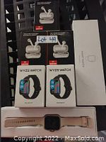 Photo showing 4 boxes of wireless earbuds, 2 boxes of Wyze smart watches, one beige band smart watch, one smart watch charger box.