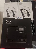 Photo showing two boxed white bladeless neck fans and a boxed black Dr.J Professional projector with control panel graphic on the box.