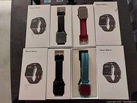 Four smart watches in white labeled boxes, each with different colored wrist straps.
