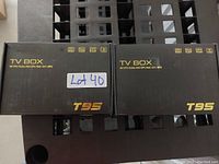 Two boxed T95 TV Boxes placed side by side on a black metal surface with vent-like holes.