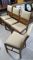 Four 1950s wooden dining chairs with beige dotted upholstered cushions, arranged in a row showing front and side views.
