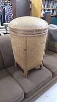 Front and side view of large woven basket with domed lid sitting on brown couch, showcasing bamboo trim and legs