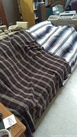 Photo showing two blankets draped side by side on a surface, one wool with plaid pattern and one striped cotton